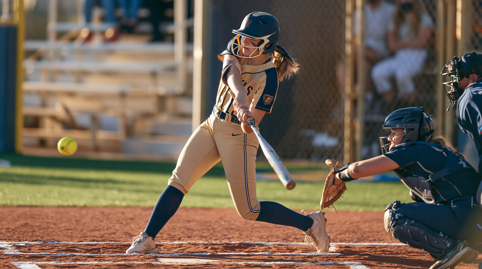 Softball batter making contact at the plate as the catcher reaches for the pitch